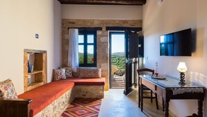 A cozy room with a stone bench, a wooden table, a TV, and a view of the outdoors. - Villa complex nearby Rethymno with stunning countryside views! (Rethymno)