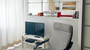 A modern living room with a flat-screen TV, a comfortable armchair, and a small table with a remote control. - Studio cabine à Arcachon centre, vue imprenable sur le bassin (ARCACHON)