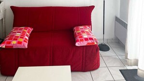 A red sofa with two patterned pillows, a white table, a floor lamp, and two landscape paintings on the wall. - Studio cabine à Arcachon centre, vue imprenable sur le bassin (ARCACHON)