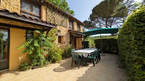 Een stenen huis met een terras, buitenmeubels en een groene parasol.