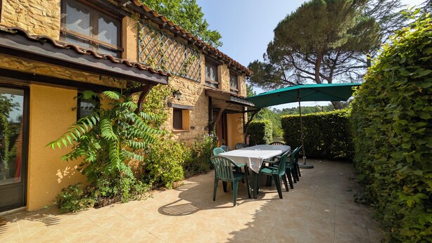 A stone house with a patio, outdoor seating, and a green umbrella. - Charming family cottage in Holiday Resort **** swimming pool, tennis, bar, etc. (Gavaudun)