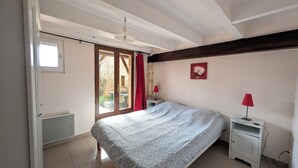 A bedroom with a bed, a nightstand, a red lamp, a wall-mounted picture, and a sliding glass door leading to an outdoor area. - Charming family cottage in Holiday Resort **** swimming pool, tennis, bar, etc. (Gavaudun)