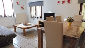 Un salon comprenant une table à manger, des chaises, un canapé, un téléviseur et une plante en pot.