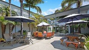 Un patio exterior con mesas, sillas, sombrillas y palmeras.