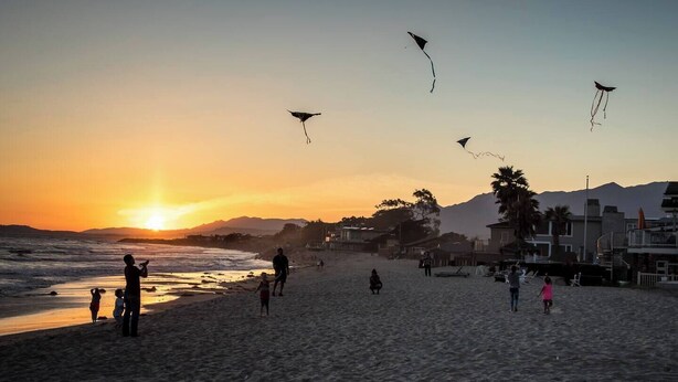 Escena de playa con gente volando cometas al atardecer.