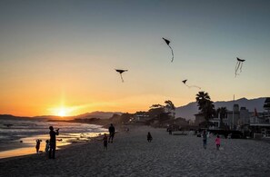 Escena de playa con gente volando cometas al atardecer.