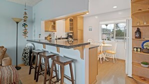 Una cocina con una isla central, taburetes de bar de madera, una zona de comedor con mesa y sillas, y vistas al exterior a través de una ventana.
