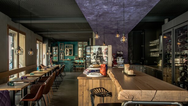 A restaurant with a long wooden bar, multiple seating areas, and hanging pendant lights. - Weinbar und Hotel FahrAway (Volkach)