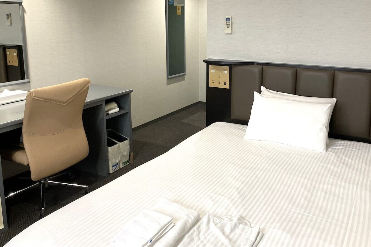 A hotel room with a bed, a desk, a chair, and a small shelf.