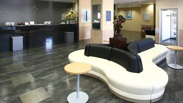 A modern lobby with a reception desk, a curved white and black sofa, and a small round table. - Shiroko Storia Hotel (Suzuka)