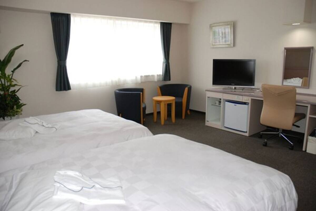 A hotel room with two beds, a desk with a computer, a TV, and a chair.