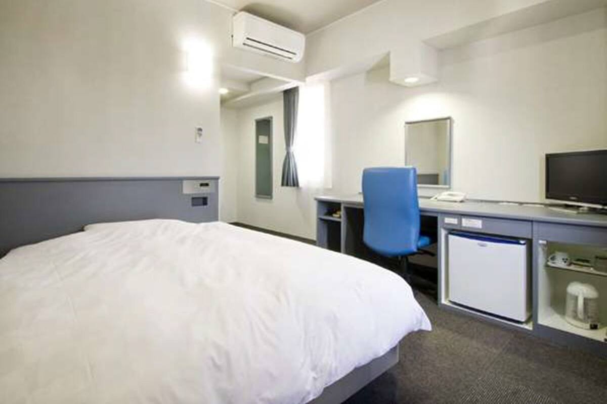 A hotel room with a bed, a desk with a chair, a television, and a minibar.