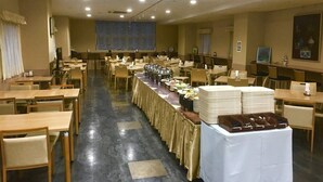 A banquet hall with multiple tables, a long table with food, and a stage in the background. - Shiroko Storia Hotel (Suzuka)