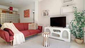 Un salon avec un canapé rouge, un meuble de rangement blanc pour appareils électroniques, un téléviseur, une table d’appoint à rayures et une plante en pot.