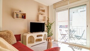 Un salon comprenant un canapé, un téléviseur, des étagères et un balcon avec des chaises.