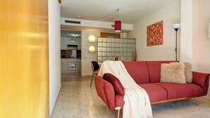 Un salon avec un canapé rouge, un plaid blanc, une lampe rouge et un tableau abstrait aux couleurs vives accroché au mur.