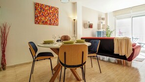 Un coin repas avec une table ronde, quatre chaises, un luminaire suspendu rouge et une peinture abstraite aux couleurs vives accrochée au mur.