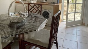 Et kompakt køkken med hvide skabe, en vaskemaskine og et spiseområde med et bord og stole.