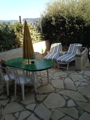 An outdoor patio with a round table, chairs, striped lounge chairs, and an umbrella.