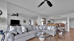 A modern living room with a sectional sofa, a glass coffee table, and a ceiling fan. - Bay Front Condo-2br/2ba , Pool, Hot Tub, Lr Balcony W/ Beautiful Sunsets, WIFI.  (Ocean City)
