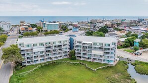 A multi-story hotel with balconies, a parking lot, and a view of the sea. - Bay Front Condo-2br/2ba , Pool, Hot Tub, Lr Balcony W/ Beautiful Sunsets, WIFI.  (Ocean City)
