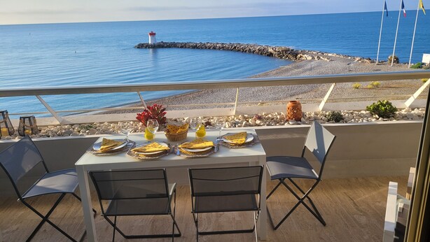 Une table dressée pour deux personnes, avec vue sur la mer et un phare en arrière-plan.
