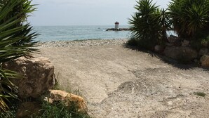 Un sentier de gravier mène à une côte rocheuse, avec un phare visible au loin.