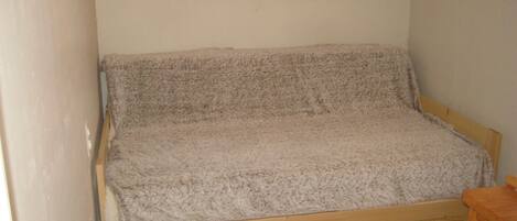 A small, single-bed room with a wooden frame and a grey blanket.