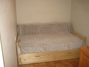 Una stanza piccola con un letto singolo, una struttura in legno e una coperta grigia.