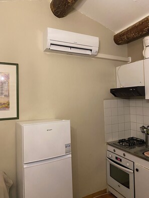 A compact kitchen with a white refrigerator, a stove, and an air conditioning unit mounted on the wall.