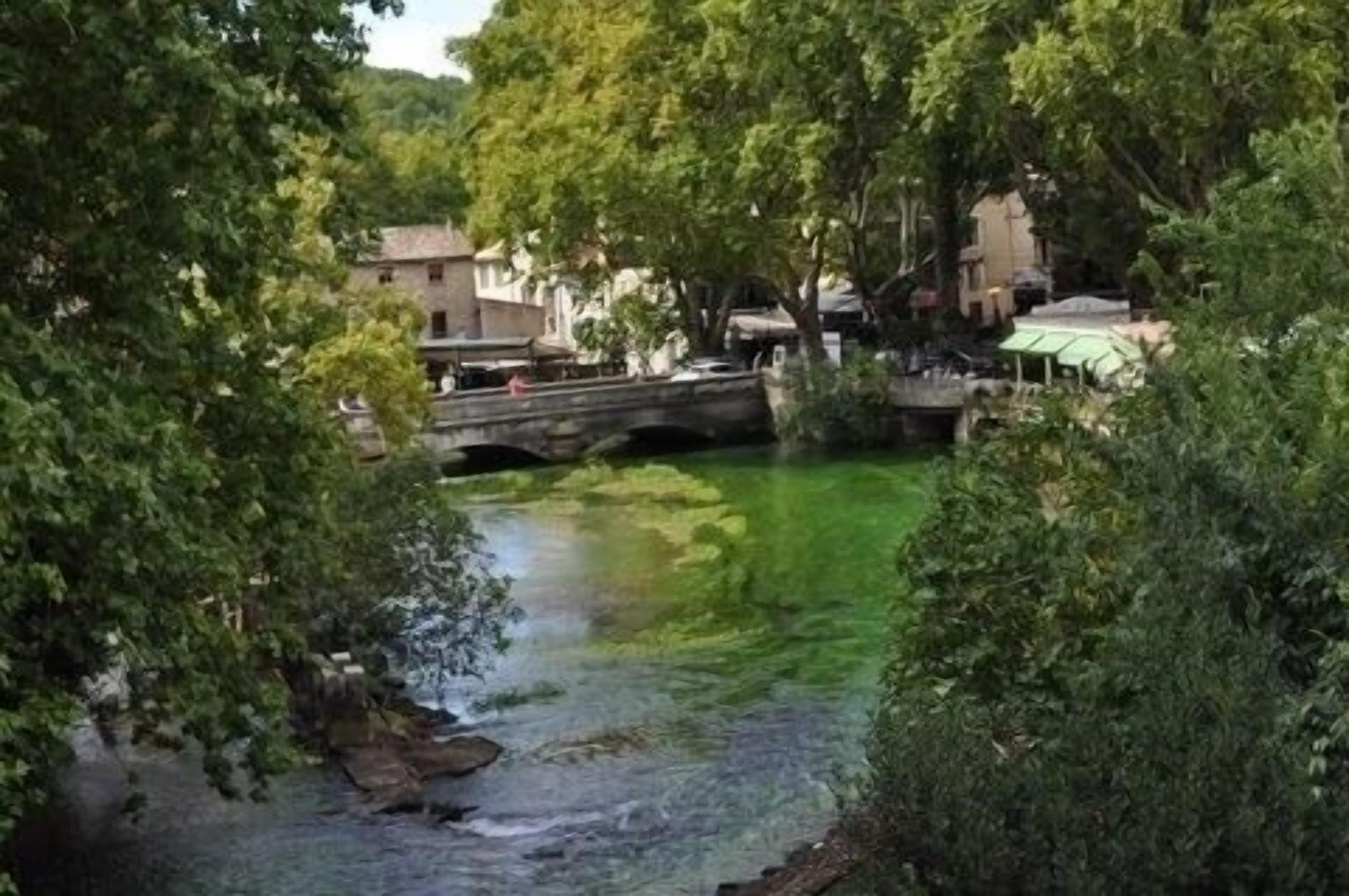 Ein Fluss mit einer Brücke, umgeben von Grünflächen und Gebäuden.