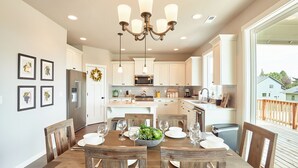 A dining area with a wooden table set for six, surrounded by wooden chairs. A chandelier hangs from the ceiling, and a large window offers a view of the outside. - So Fresh & So Clean - A Brier Maison Luxury Rental (Dundee)