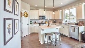 A modern kitchen with white cabinets, stainless steel appliances, and a large island with stools. - So Fresh & So Clean - A Brier Maison Luxury Rental (Dundee)