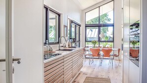 Une cuisine moderne dotée d’une grande fenêtre, de meubles en bois et d’un coin repas avec des chaises orange.
