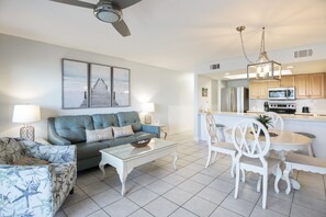 Uma sala de estar moderna com sofá, mesa de centro e mesa de jantar. Há uma área de cozinha com geladeira, micro-ondas e armários.