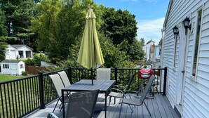 Een houten terras met tuinmeubilair, zoals een tafel, stoelen en een barbecue.