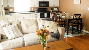 Een woonkamer met een beige bank, een houten salontafel en een vaas met bloemen.