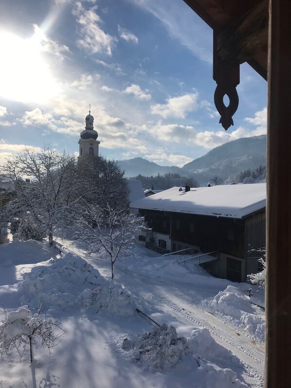 A snow-covered landscape with a church and buildings, a clear sky, and mountains in the background.