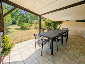 An outdoor patio with a table and chairs, surrounded by a tiled floor and a covered area.