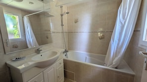 A bathroom with a bathtub, a sink, a mirror, and beige tiles.