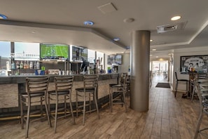 A bar area with wooden flooring, bar stools, and a television displaying a sports game.