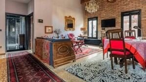 Una sala de estar acogedora con un sofá de madera, una mesa de comedor con sillas rojas, una araña y un espejo grande en la pared.