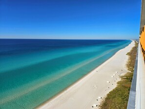 An aerial view of a beach with clear turquoise waters, a sandy shore, and a building on the right. - Beachfront Luxe @ Splash 1203E • Fireplace • Recliners, Free Beach Chairs, Crib! (Panama City Beach)