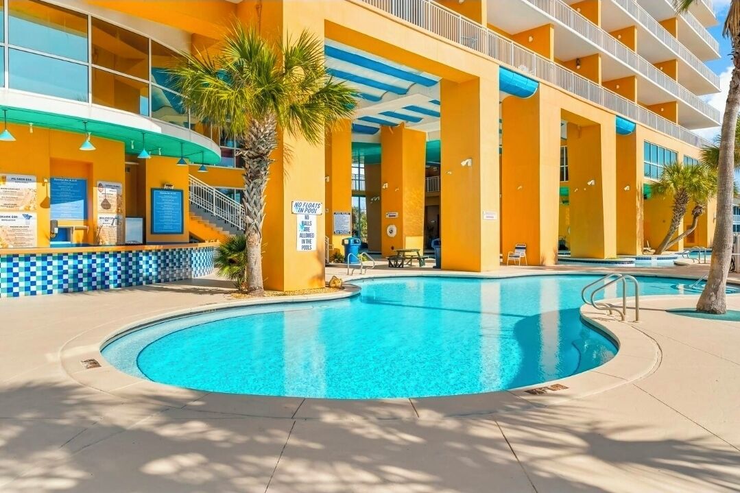 Un hotel con zona de piscina, palmeras y un cartel que indica que no se permiten flotadores en la piscina.