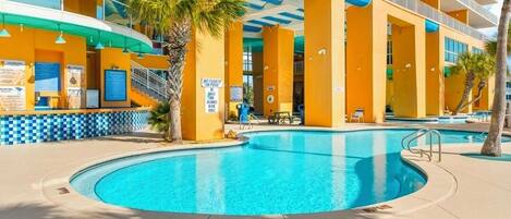 Un hotel con zona de piscina, palmeras y un cartel que indica que no se permiten flotadores en la piscina.