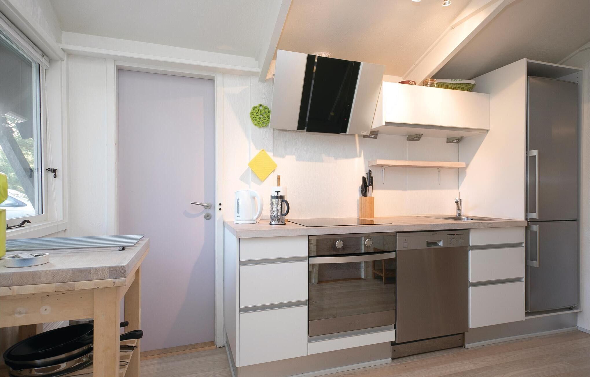 Eine moderne Küche mit weißen Schränken, einem eingebauten Ofen, einem Edelstahl-Kühlschrank und einem Fenster mit Jalousien.
