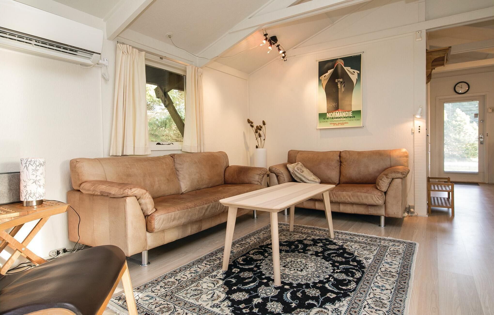 A living room with two sofas, a coffee table, a patterned rug, a poster on the wall, and a window with curtains.