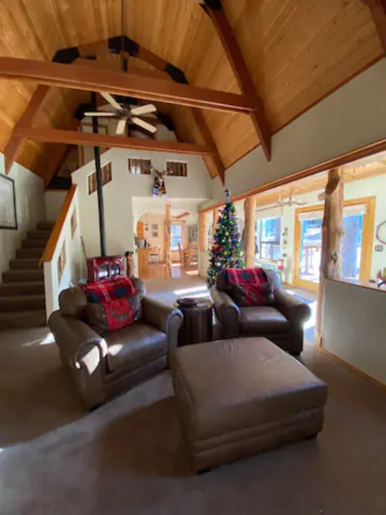 A spacious living area with a high wooden ceiling, a staircase, and a Christmas tree.