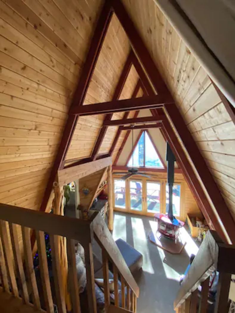 A wooden interior with a sloped ceiling, a staircase, and a view of the outside.