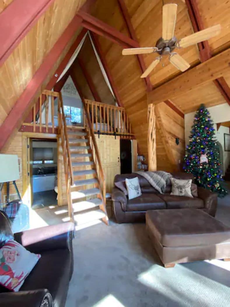 Ein Holzinnenraum mit Treppe, einer Couch, einem Weihnachtsbaum und einem Deckenventilator.